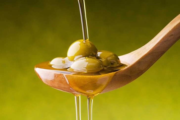 extra virgin olive oil flows on a wooden bowl full of green olives