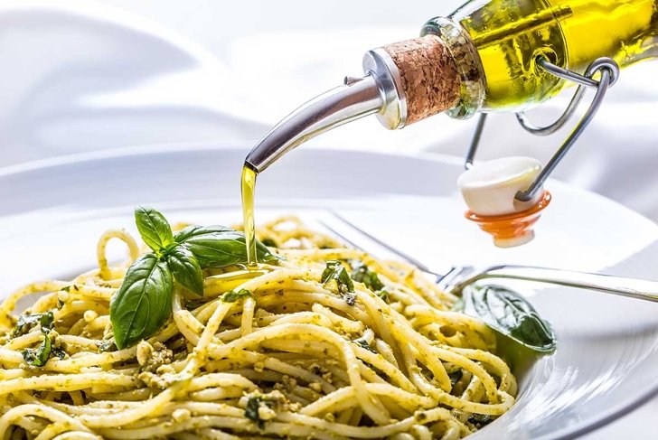 Spaghetti with homemade pesto sauce pouring olive oil and basil leaves.