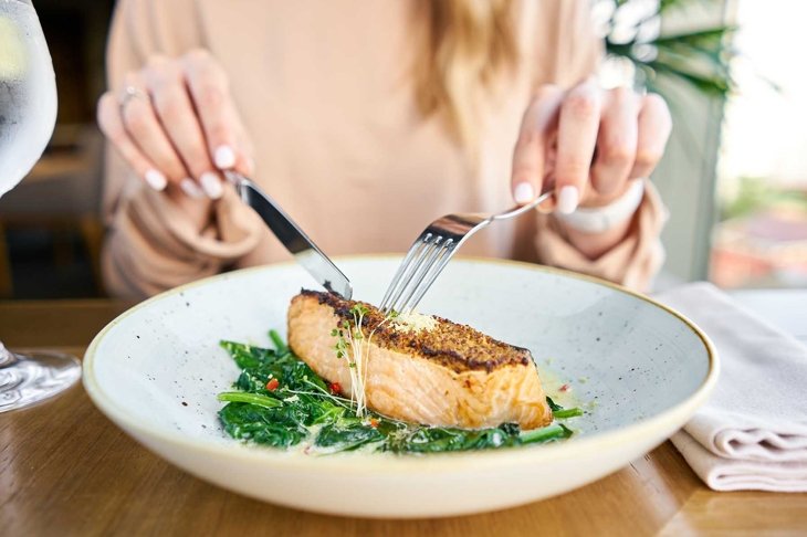 Salmon steak fillet with grainy mustard and spinach. Lunch in a restaurant, a woman eats delicious and healthy food. Restaurant menu, a series of photos of different dishes