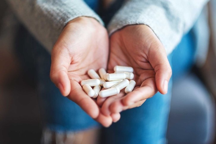 Closeup image of a woman holding white medicine capsules in hands